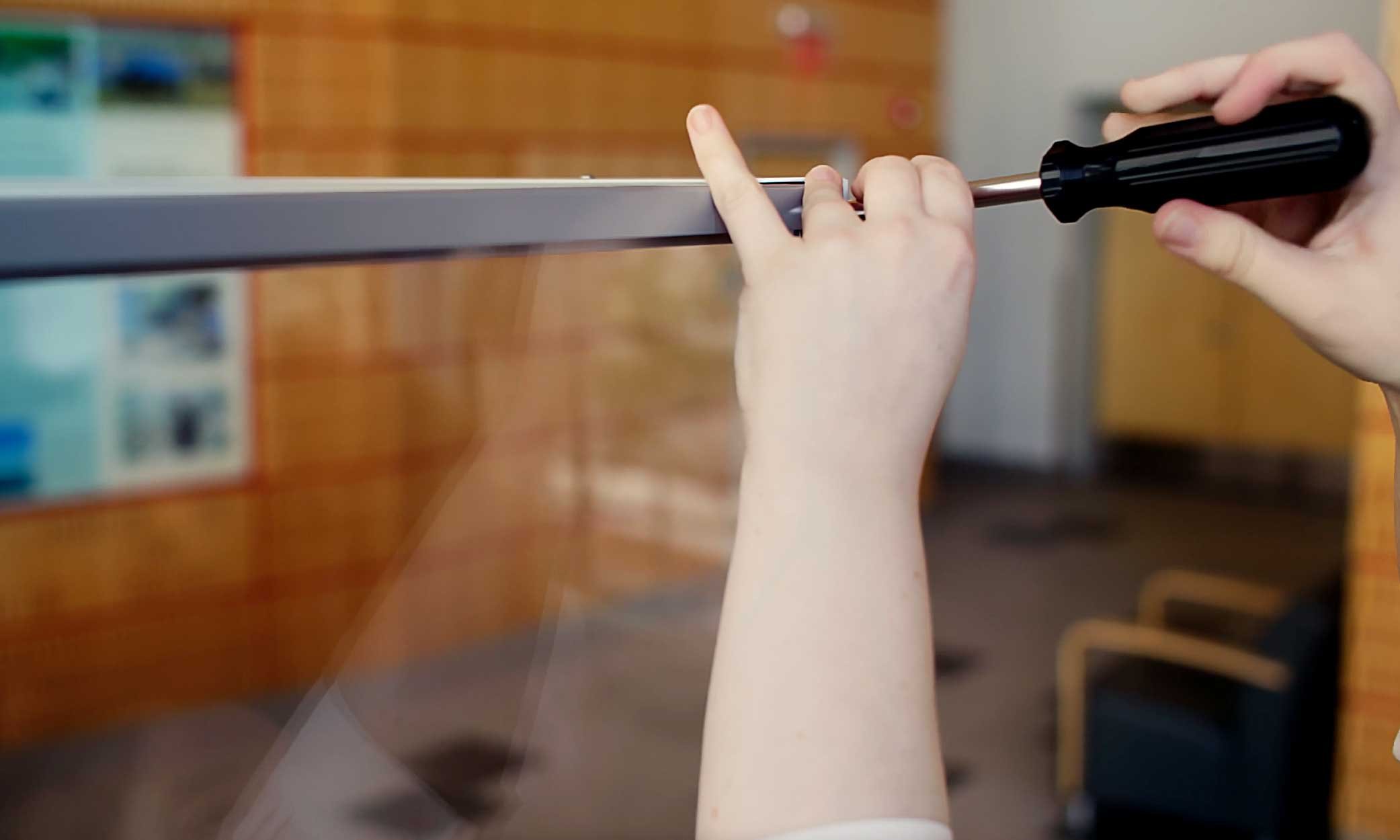 Hand holding a screwdriver, removing a screw from a panel